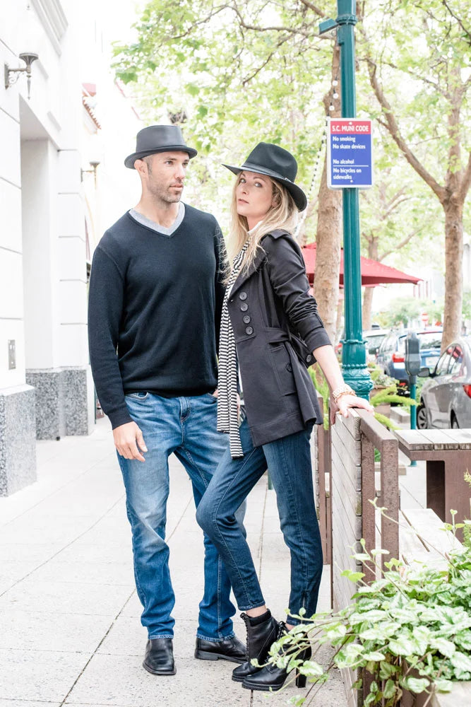 A man and a woman standing on a sidewalk wearing black hats