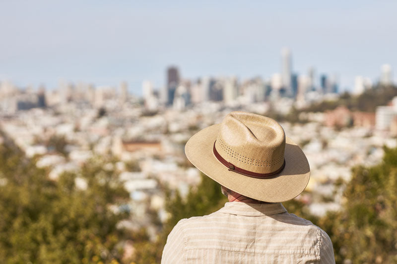 A man on an overlooking view wearing a tan straw sun hat