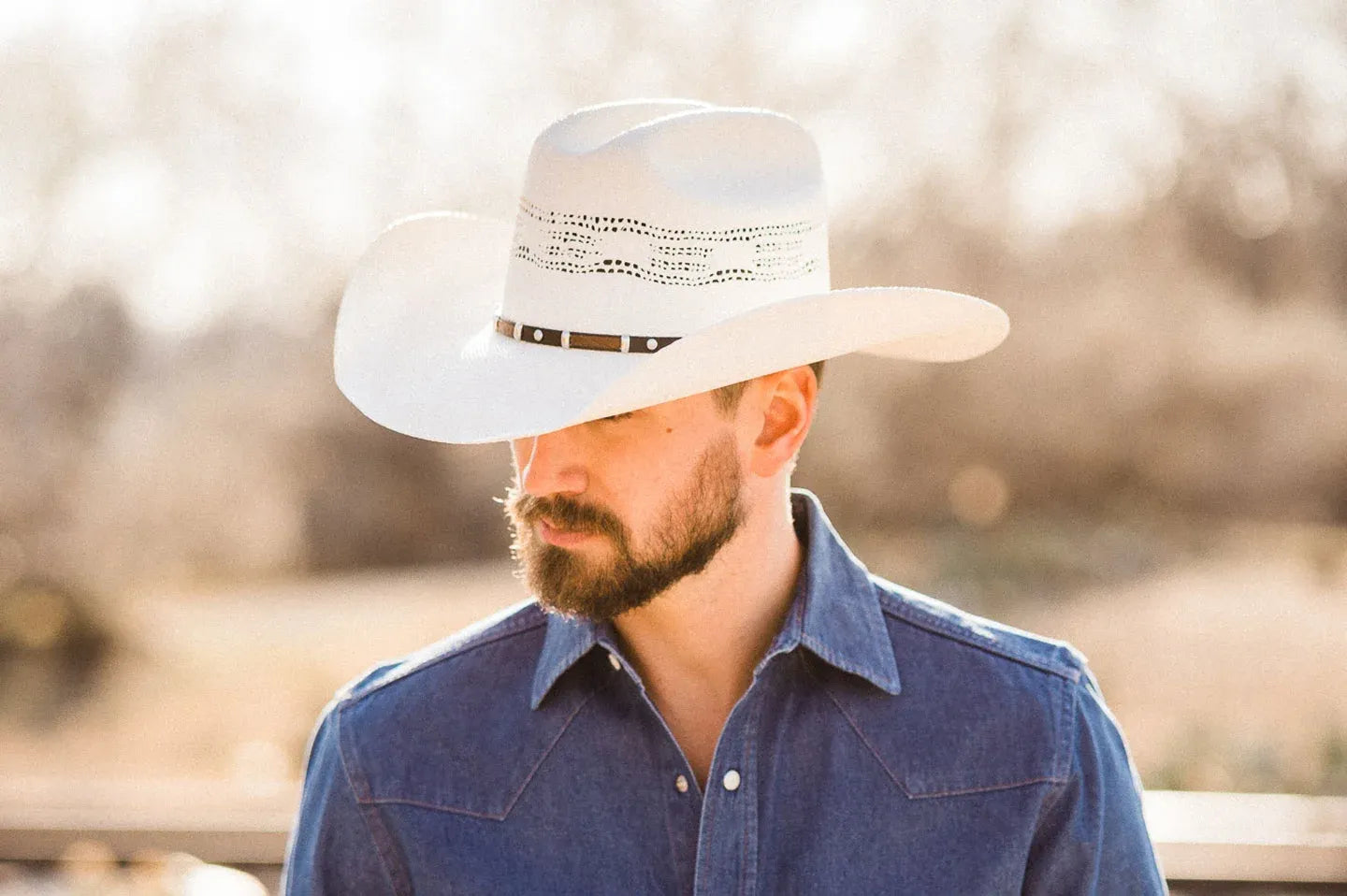 A young man in a denim jacket and a cream cowboy hat