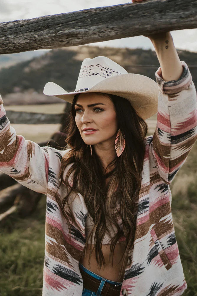 A woman standing outdoors wearing a tank top with a sweater and a straw cowboy hat