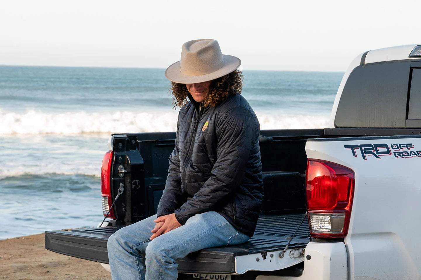 man in a black jacket sitting at the back of the car wearing sun festival hat by american hat makers