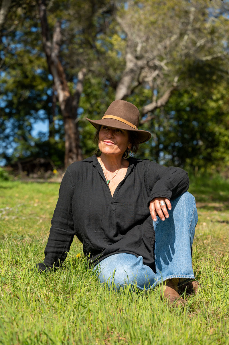 A woman sitting on the grass wearing a brown felt fedora hat