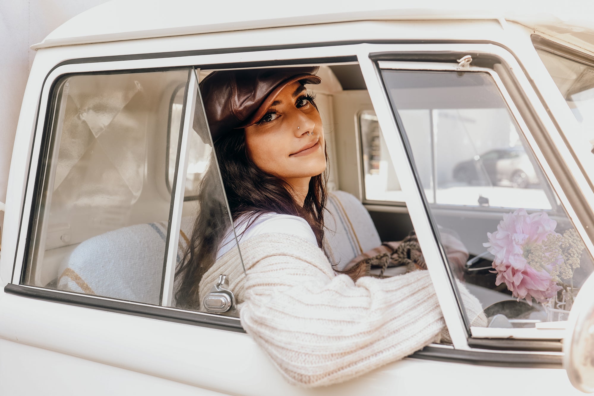 A young woman sitting inside a car wearing a leather cap