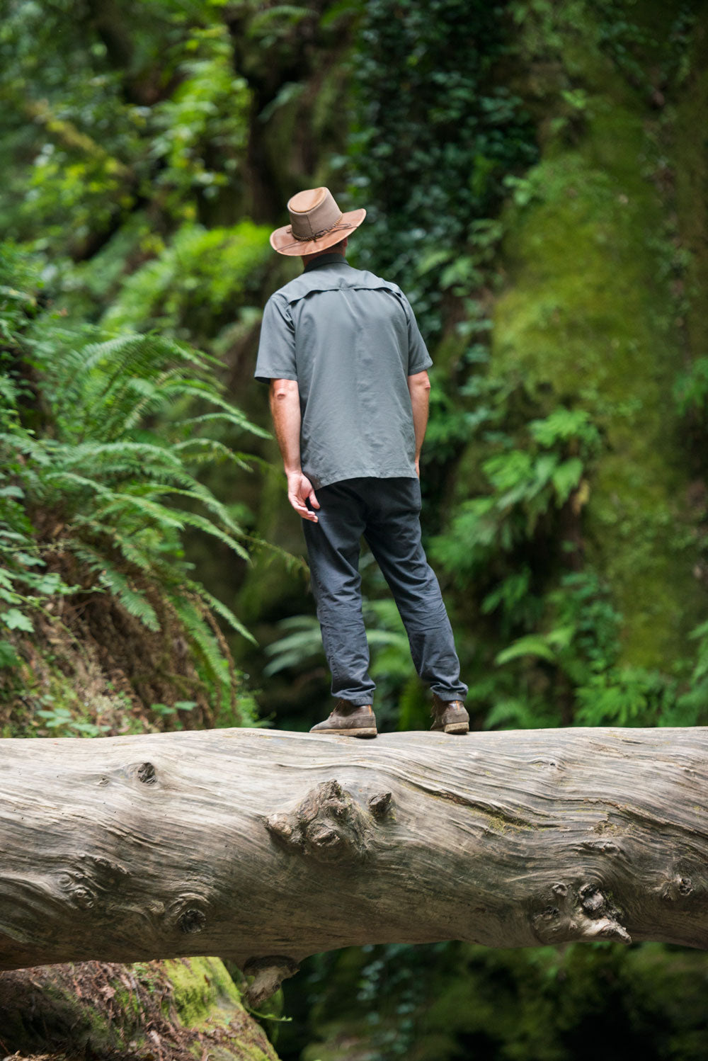 A man standing on a timber bridge wearing  jeans and a sunhat