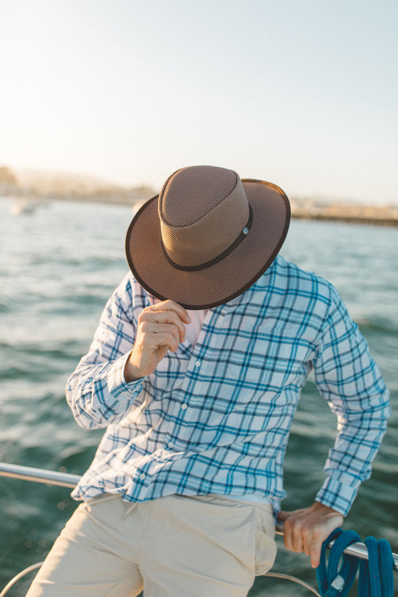 A man on a boat wearing a checkered blue polo and a cabana walnut sun hat