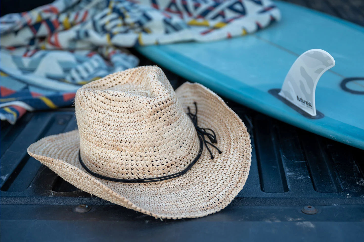 A Blue surf board beside a Brown straw cowboy hat by American Hat Makers
