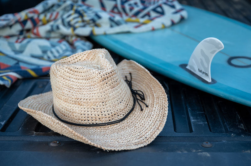 A calder straw cowboy hat placed beside a surf board