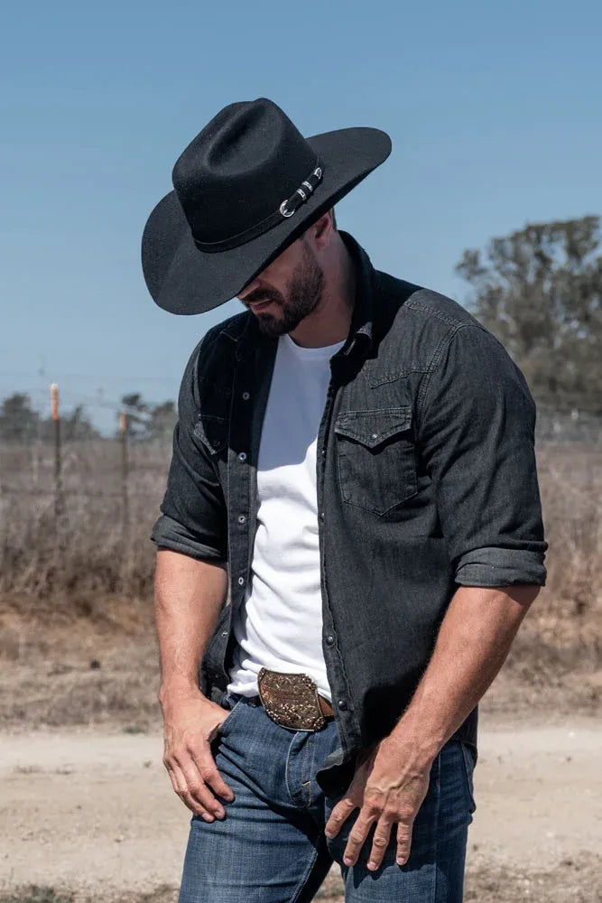 A man in a farm wearing a black jacket and a felt cowboy hat