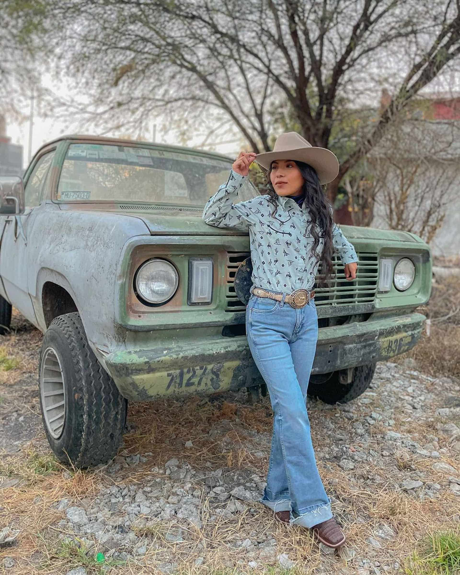 A curly haired woman wearing a sand felt hat with polo and jeans standing in front of a truck