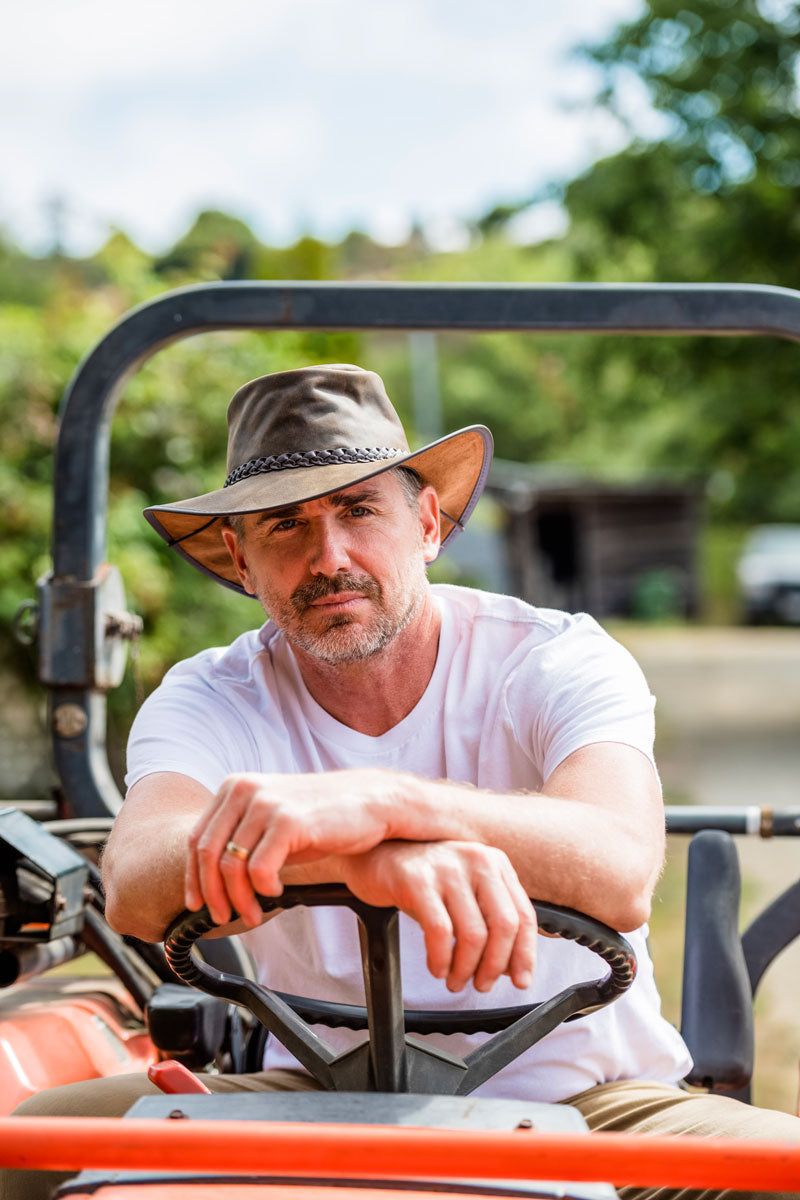 A man sitting on a cart wearing a bomber brown leather hat