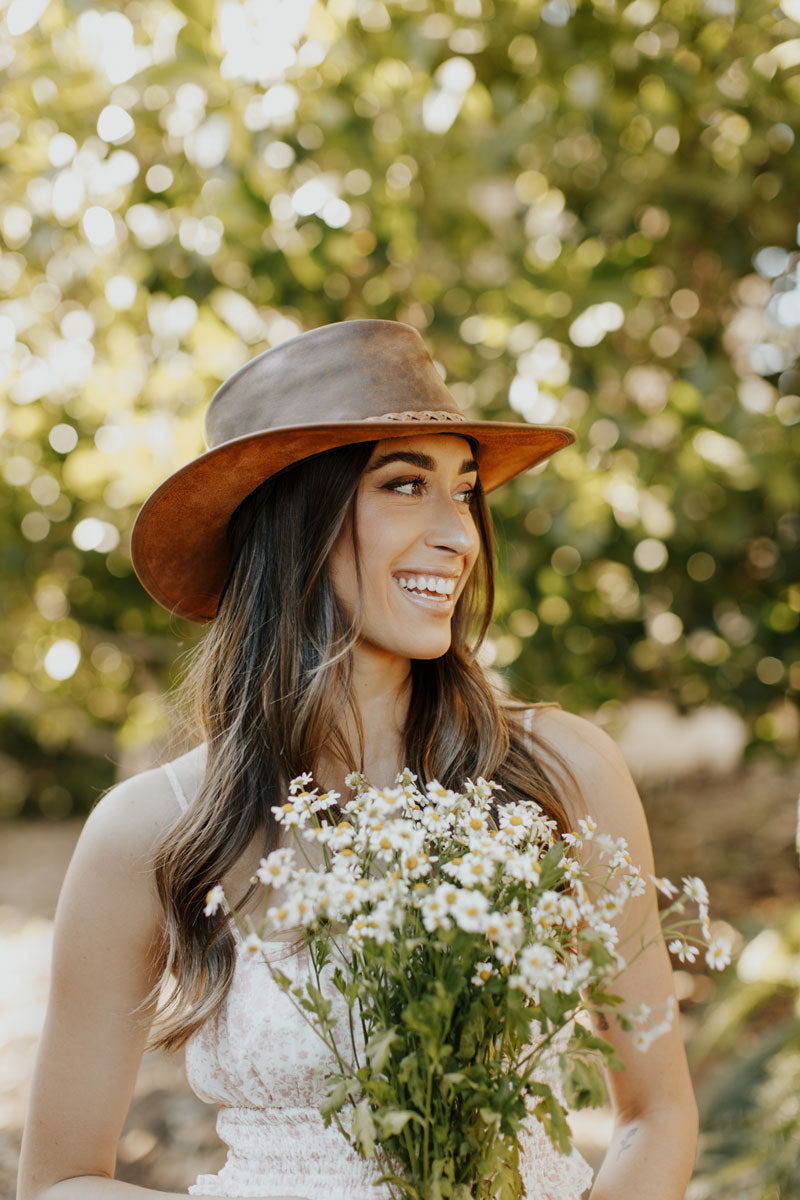 A woman wearing white dress and a copper leather hat