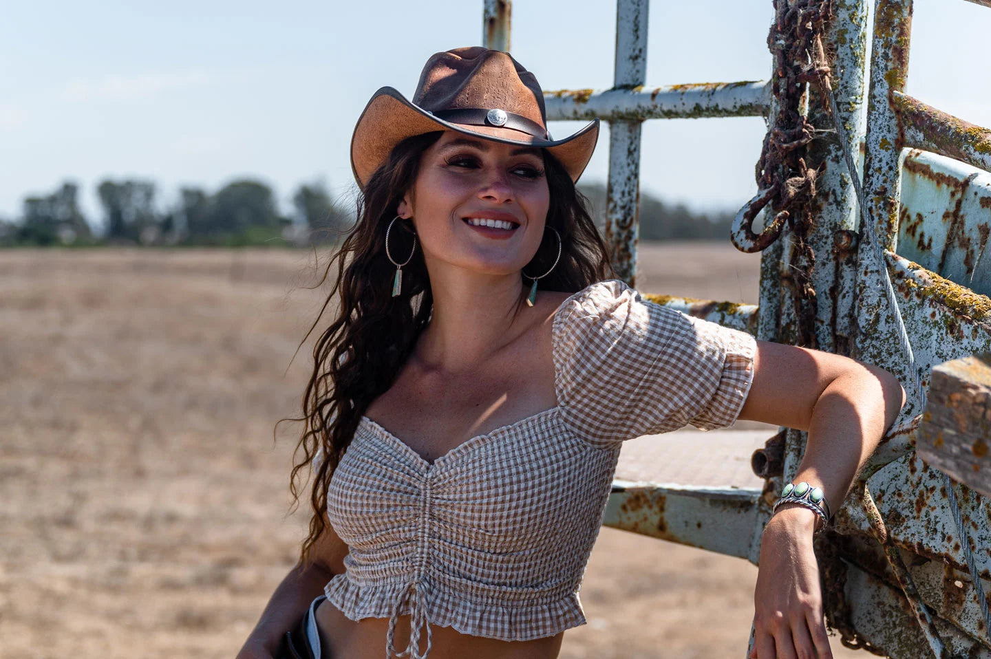 woman leaning at the back of the truck outside the field wearing a brown leather hat by american hat makers