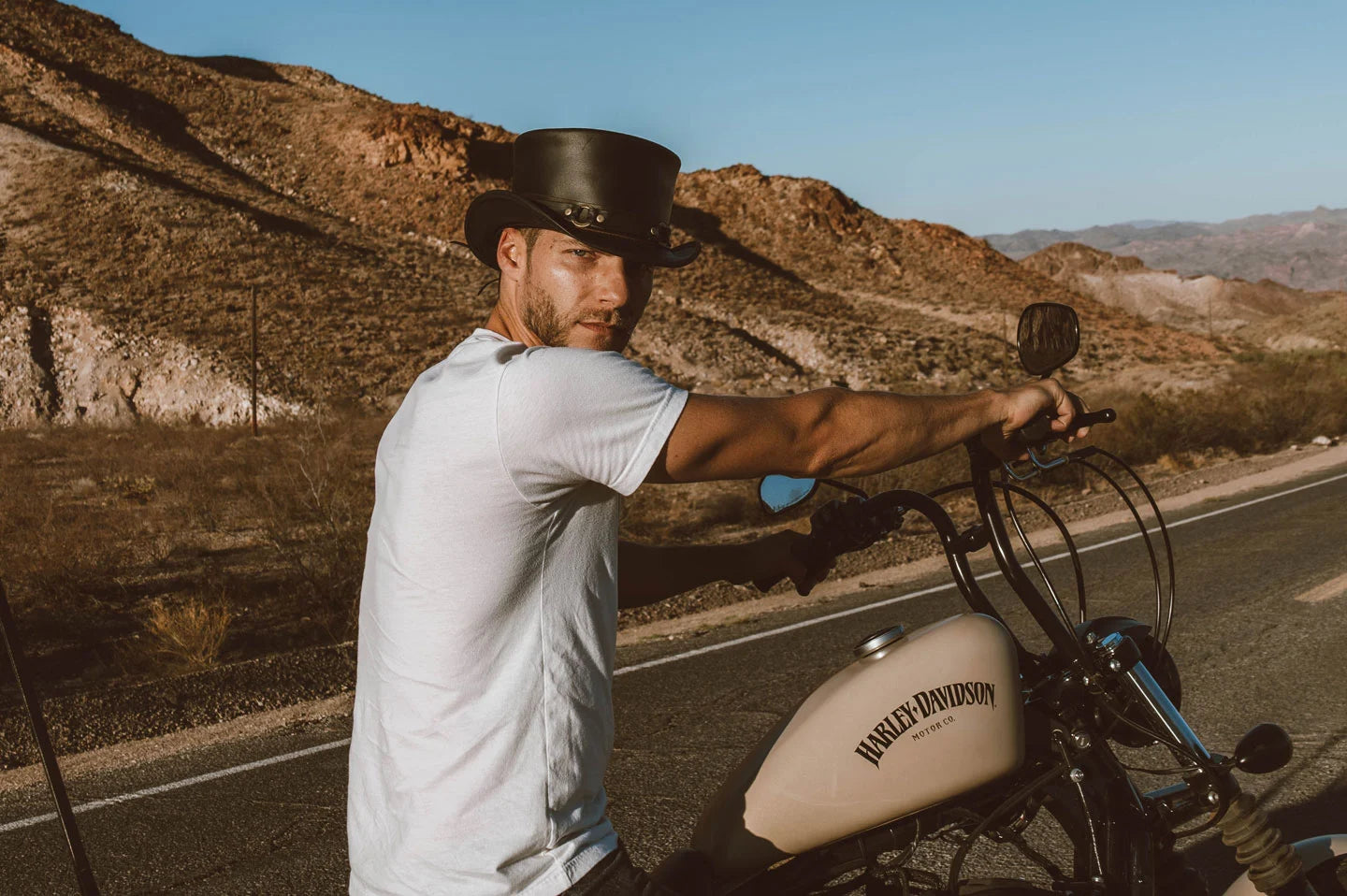 man on a harley davidson on riding on the highway wearing a white shirt and black top hat