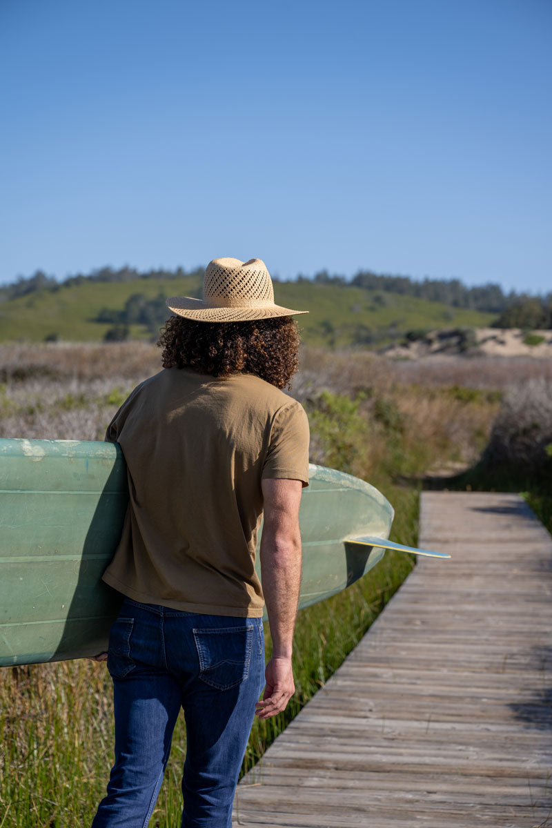 A man holding a surf board wearing a straw sun hat