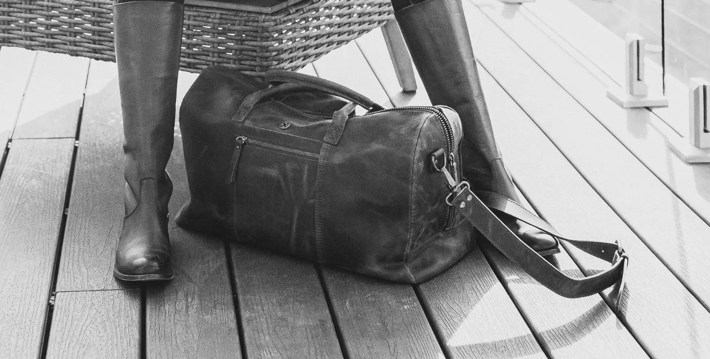 A leather bag placed on a wooden floor in between a person's legs