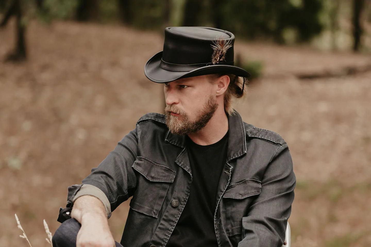 man in a black jacket sitting outside wearing a voodoo top hat by american hat makers