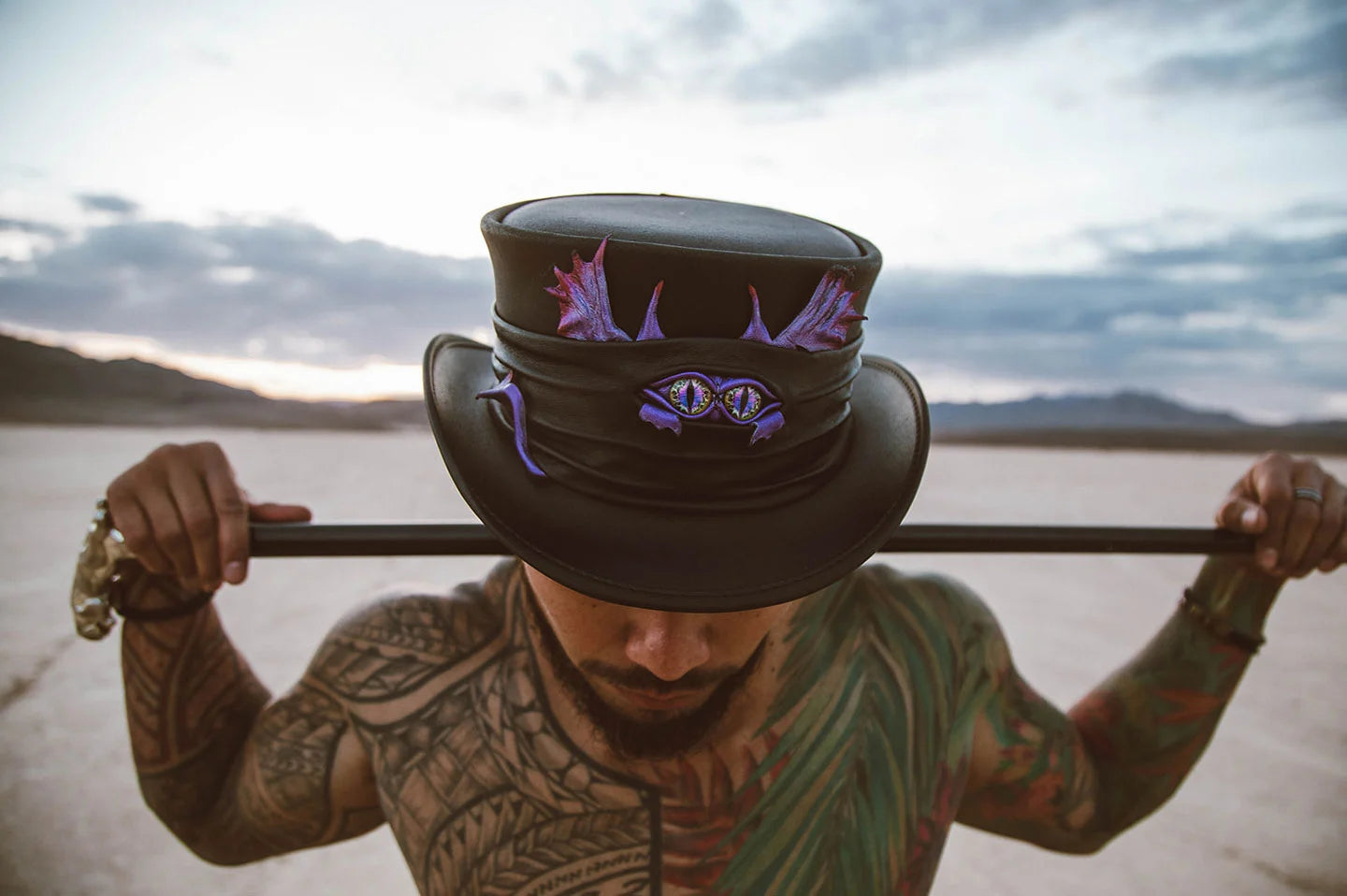 tattooed man with a cane wearing a black leather steampunk top hat