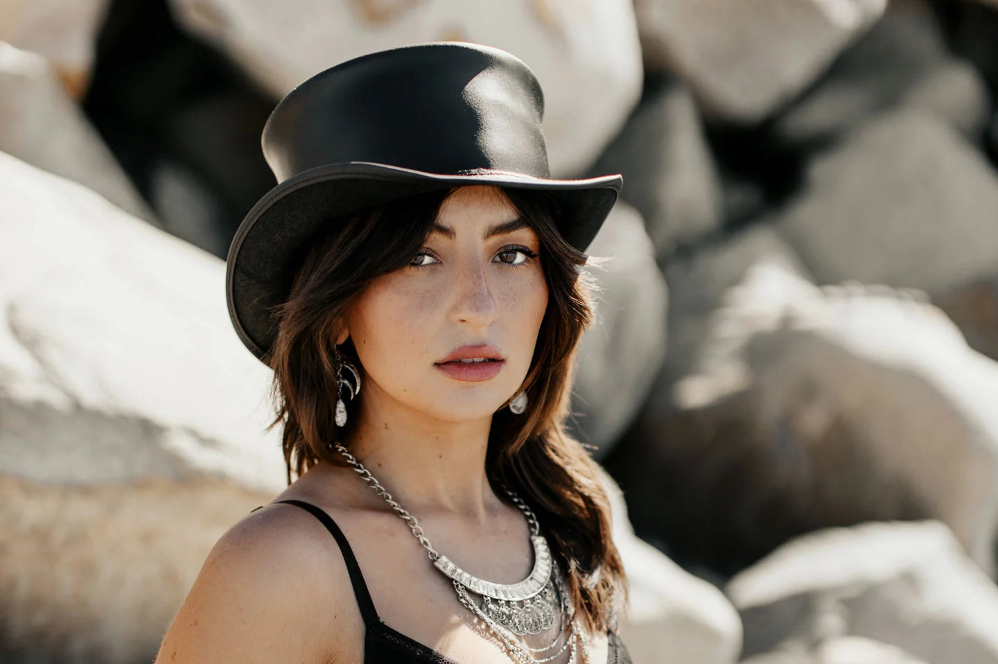 woman in black standing outside full of rocks wearing voodoo top hat by american hat makers