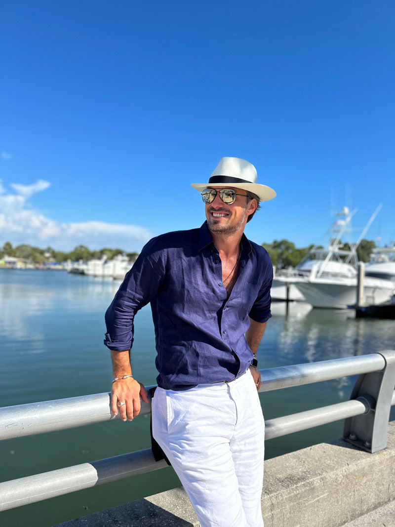 A man leaning on the bridge wearing a blue polo and a white straw sun hat