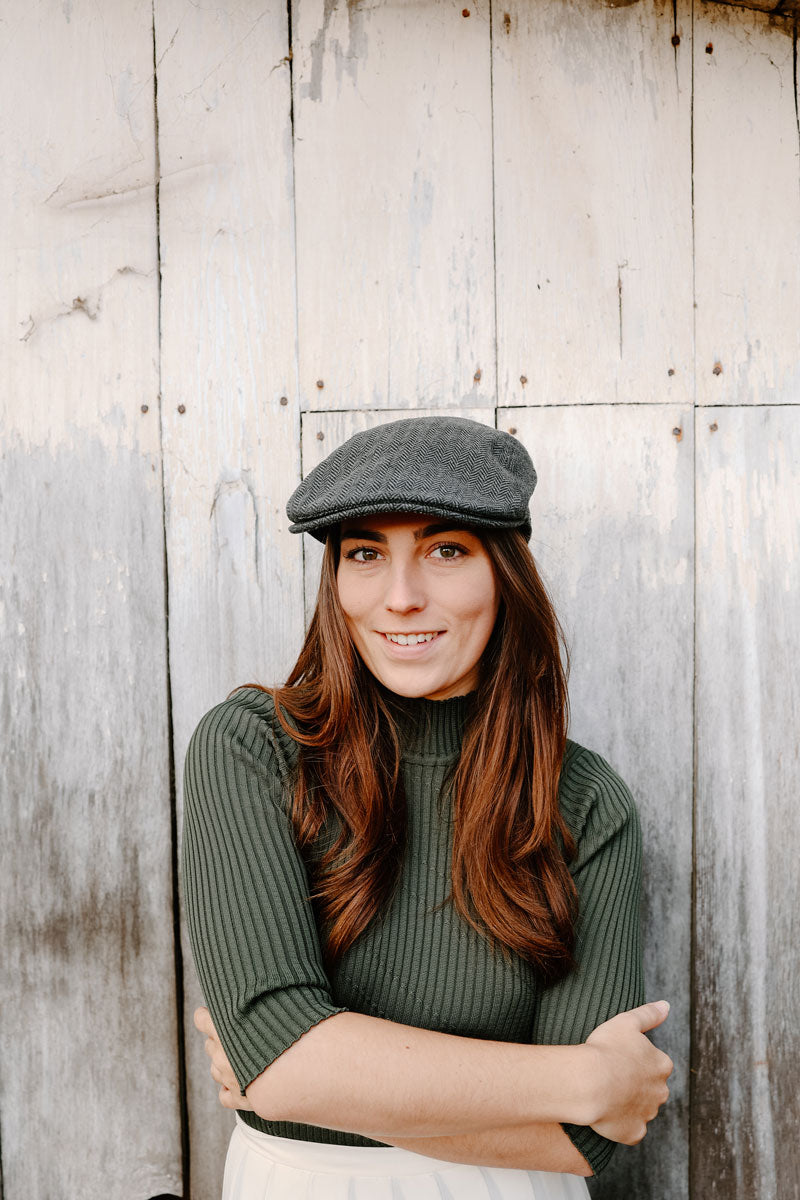 A woman leaning on a wall wearing a mikey charcoal cap