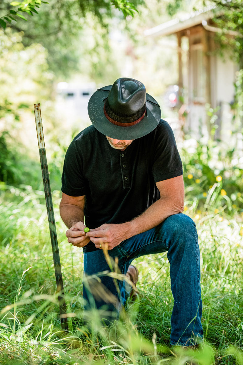 A man kneeling down on a grass wearing a black sun hat