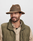 Smiling man wearing a brown Otis leather hat and a green outdoor jacket over a beige shirt.
