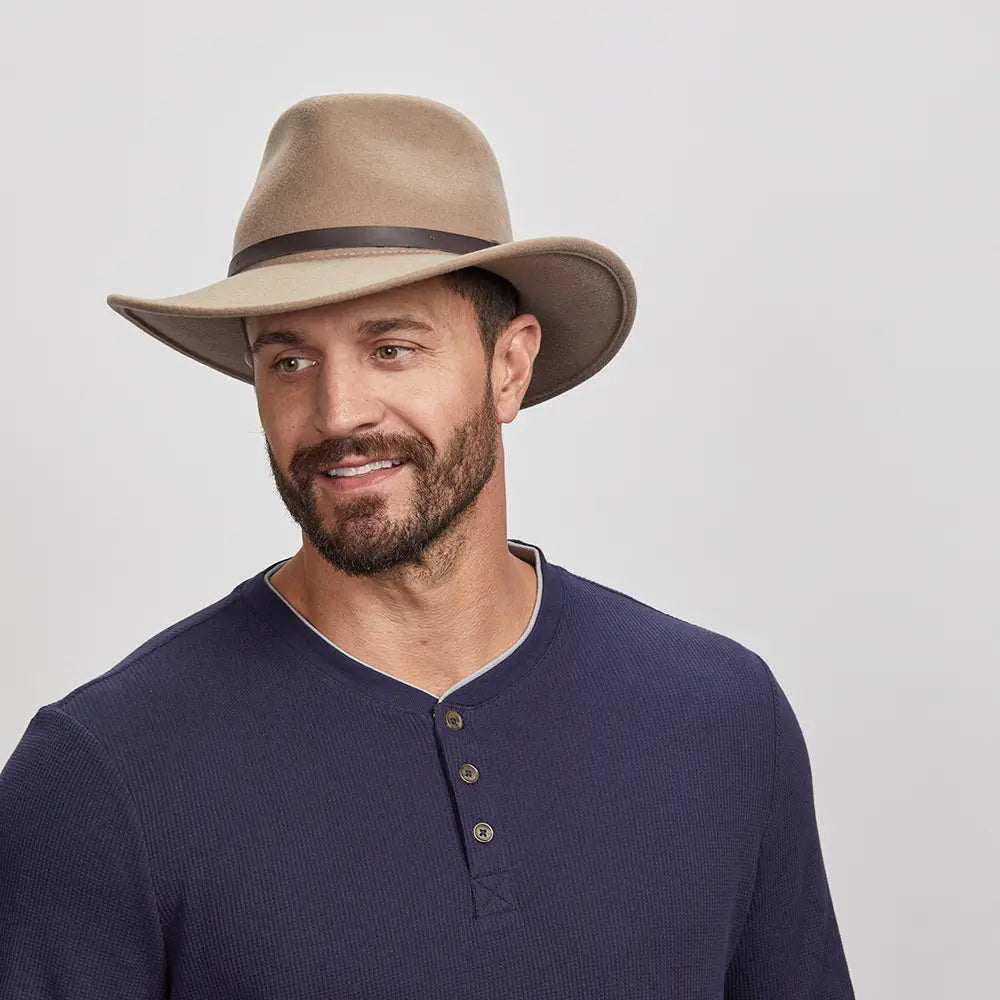 Man in a putty Pathfinder Fedora and navy blue henley shirt giving a subtle smile