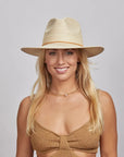 Portrait of a smiling woman with blonde hair wearing a Paulo straw hat and a brown knitted top.