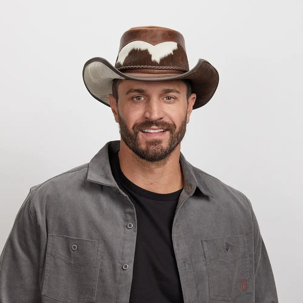 Smiling man wearing a distinctive brown Pinto leather hat, styled with a grey button-up shirt.