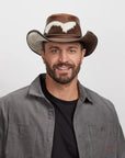 Smiling man wearing a distinctive brown Pinto leather hat, styled with a grey button-up shirt.