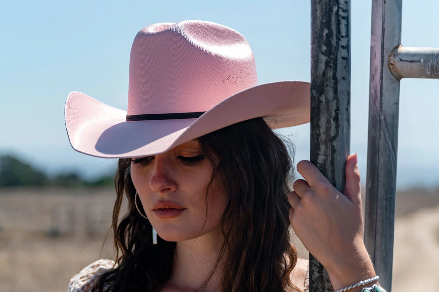 woman with a curly hair outside the field wearing a pink hat by american hat makers