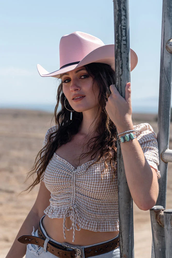 cowgirl leaning against fence wearing the Pioneer cowgirl hat by American Hat Makers