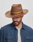 Man in a blue shirt wearing a brown Ralston hat, looking downward