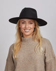 Woman with long blonde hair wearing a beige turtleneck sweater and a black Rancher hat.