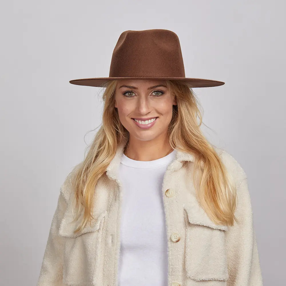 A woman with long blonde hair, smiling and wearing a brown Rancher hat and a textured cream coat over a white shirt