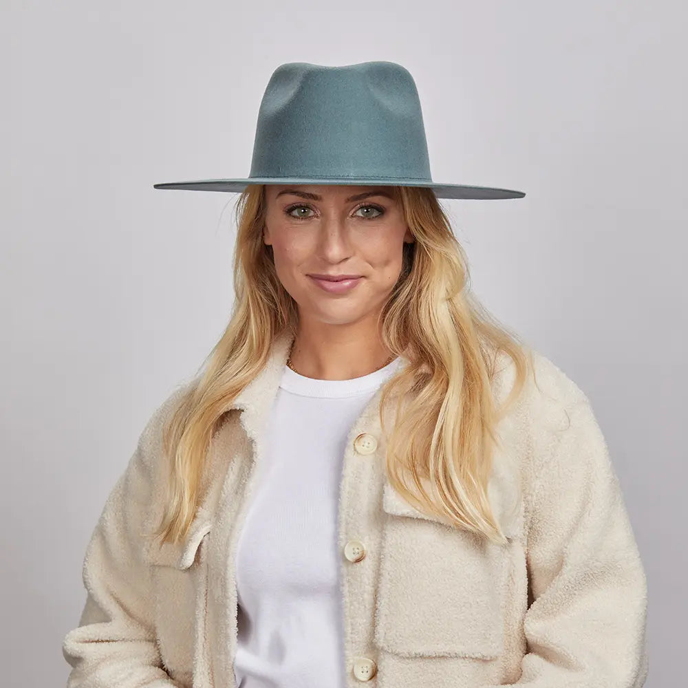 A smiling woman wearing a green Rancher hat and a cream textured jacket over a white top.