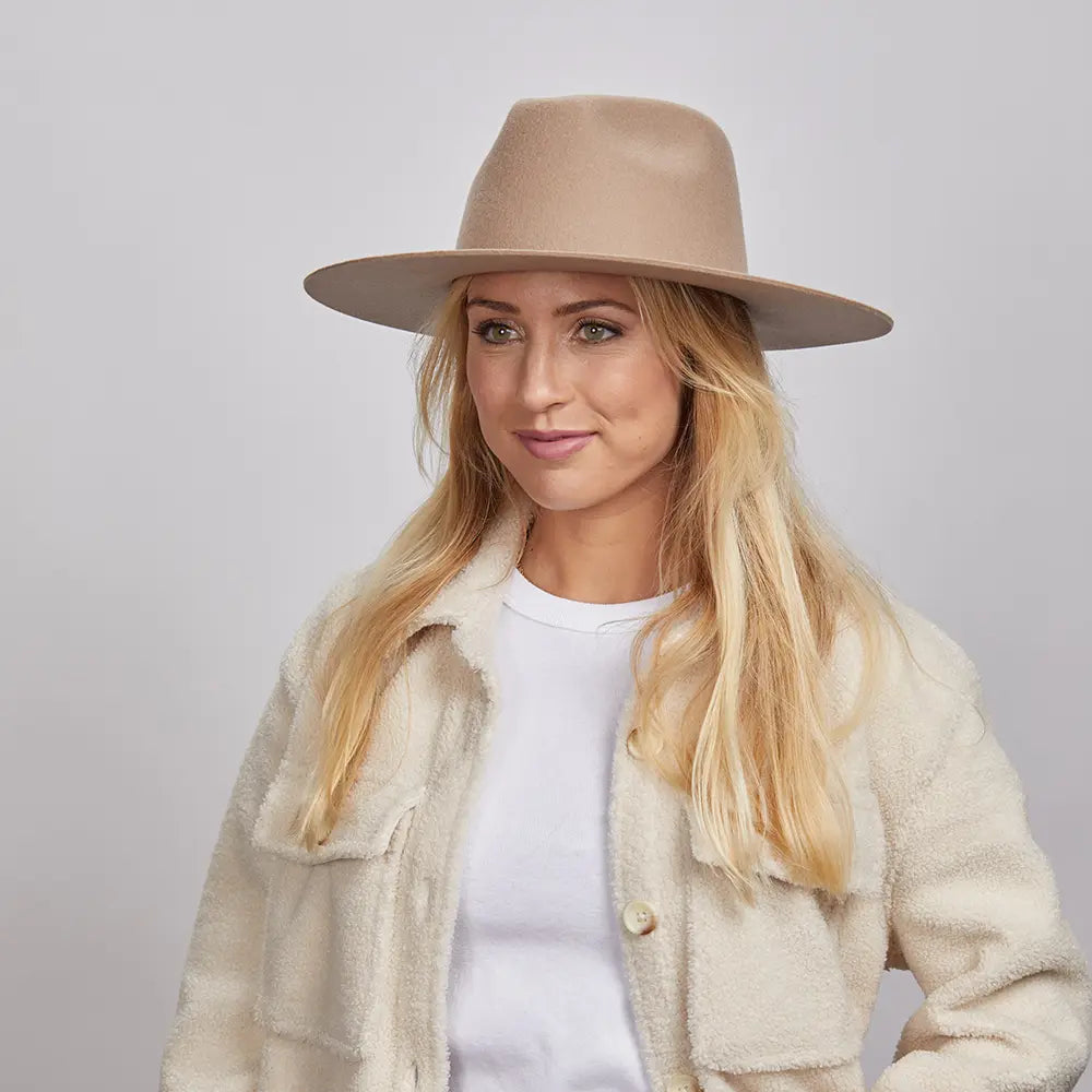 A woman with long blonde hair, smiling and wearing a tan Rancher hat and a textured cream coat over a white shirt.
