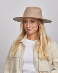 A woman with long blonde hair, smiling and wearing a tan Rancher hat and a textured cream coat over a white shirt.
