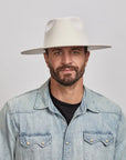 Man with a beard wearing a White Rancher Hat and a denim jacket over a black shirt.
