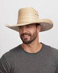 A smiling man looking to the side wearing a straw cowboy hat