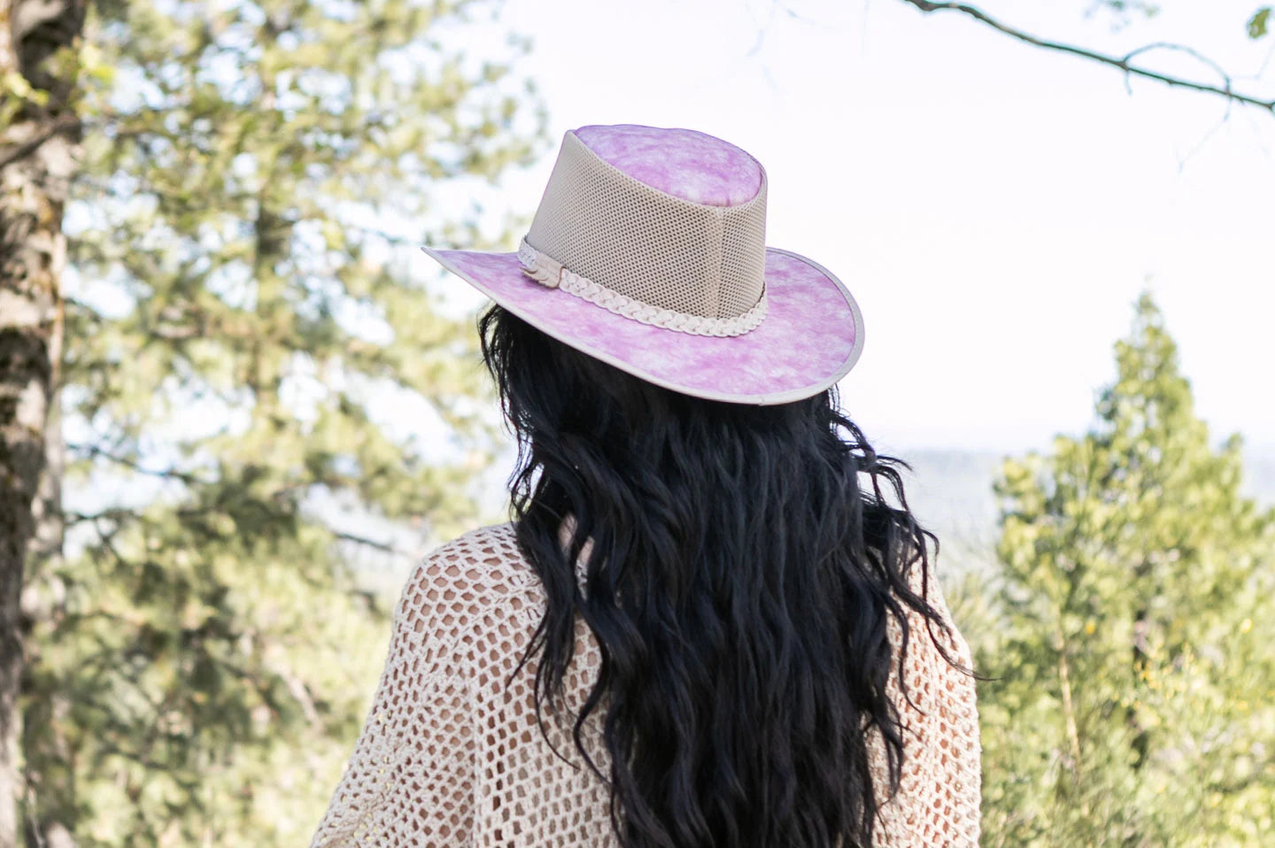 woman with a long black curly hair looking at the trees wearing a pink hat by american hat makers