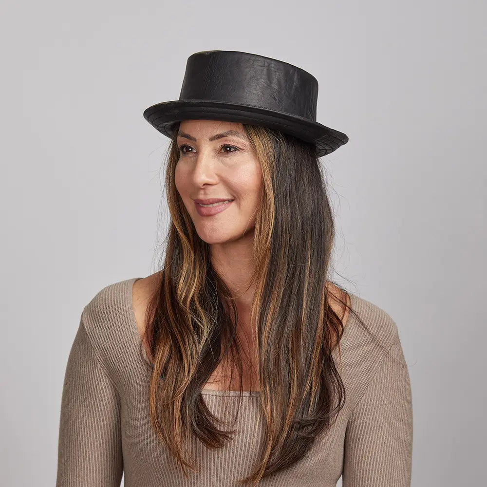 A woman with long brown hair wearing a Black Rumble Leather Hat and a beige sweater.