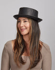 A woman with long brown hair wearing a Black Rumble Leather Hat and a beige sweater.