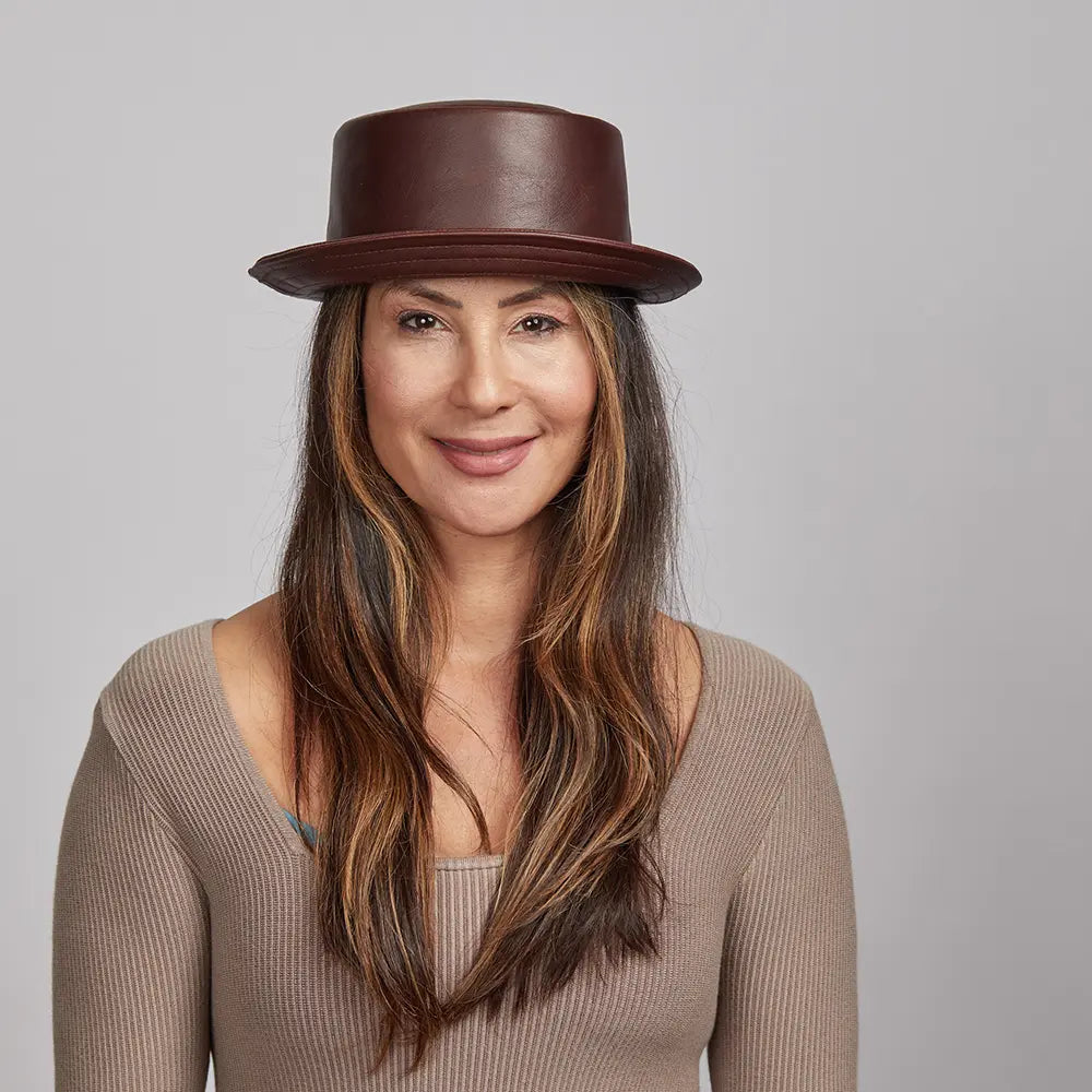 A woman with long brown hair wearing a Brown Rumble Leather Hat and a beige sweater.