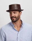 A young man looking to the side wearing a brown leather hat