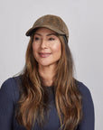 A woman slightly smiling wearing a brown leather cap and a navy blue top