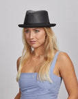 A woman with blonde hair wearing a black leather hat and a blue sleeveless looking to the side