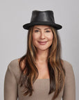 Woman with long brown hair wearing a black leather hat and a beige top, smiling