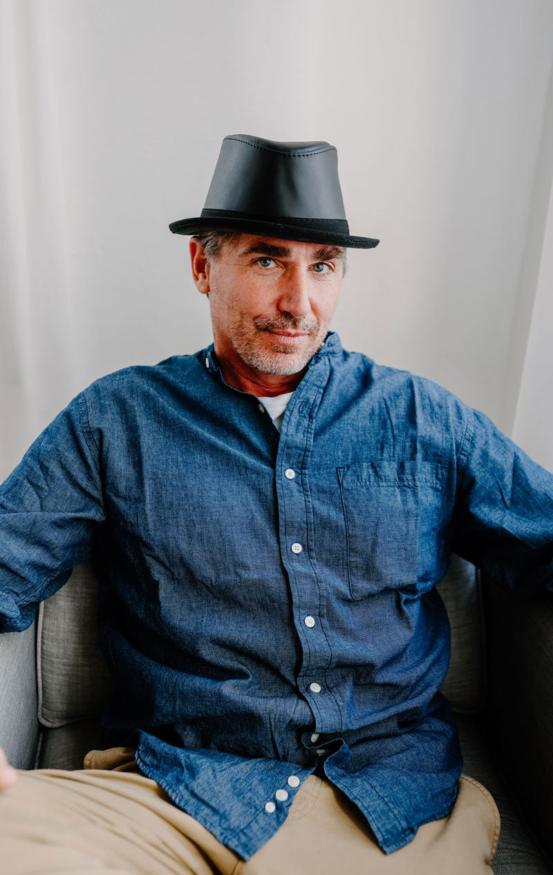 A man sitting down wearing a black leather hat