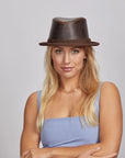 A woman with blonde hair wearing a brown leather hat and a blue sleeveless top